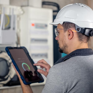 Técnico de infraestructura de TI revisando tablero eléctrico y monitoreando datos en una tablet
