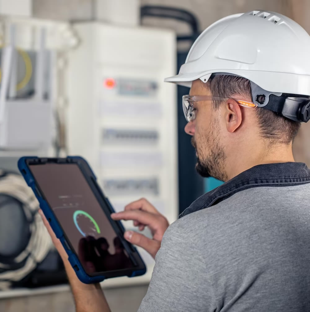 Técnico de infraestructura de TI revisando tablero eléctrico y monitoreando datos en una tablet